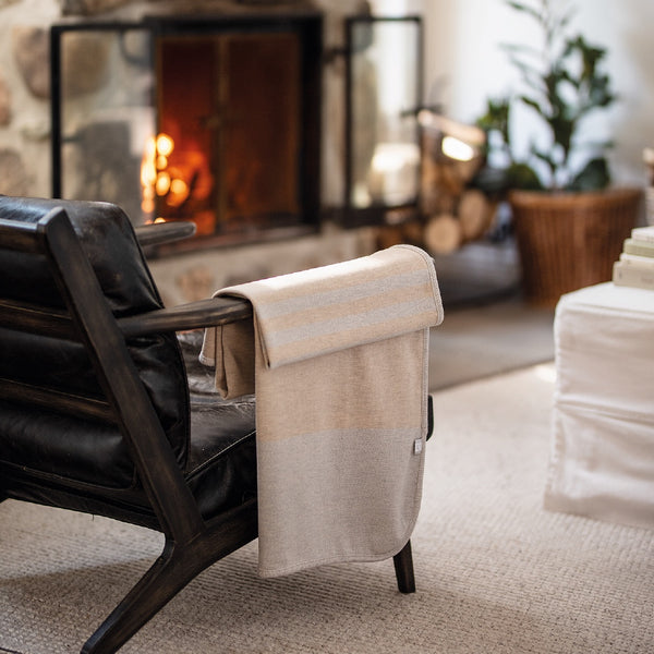 Jeté beige en laine de mérinos devant foyer / Beige merino wool throw in front of fire place made in Canada by Volprivé.