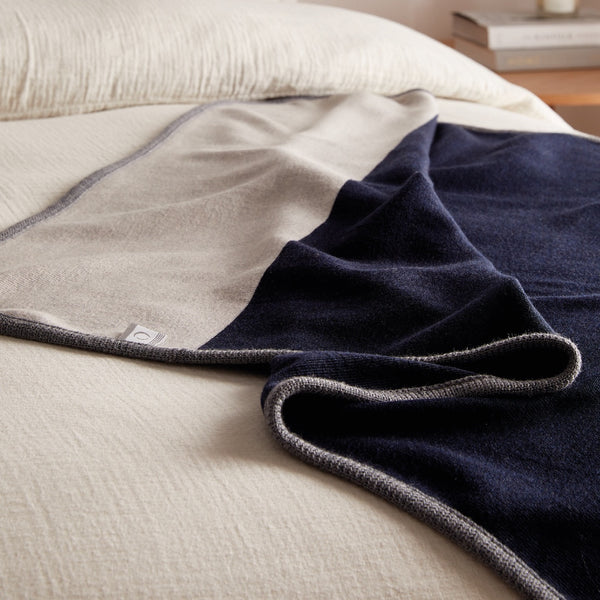 Gros plan jeté bleu marine en laine de mérinos sur lit / Close up of a navy blue merino wool throw on bed made in Canada by Volprivé.