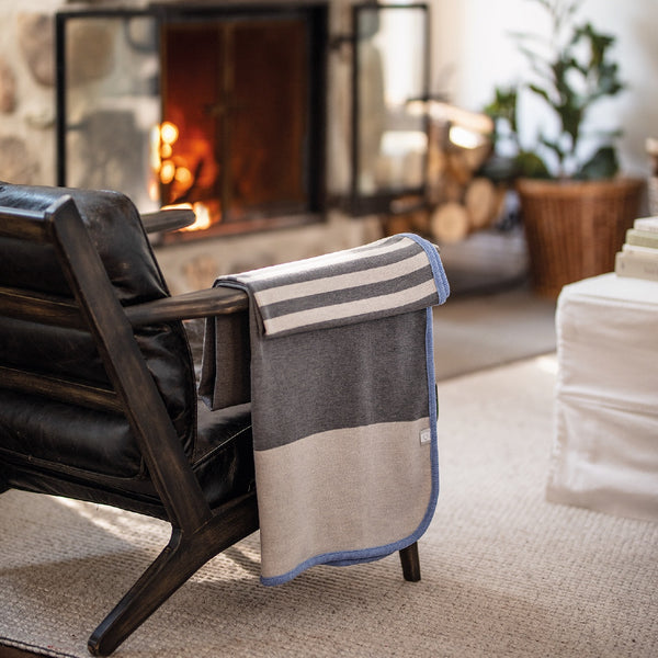 Jeté gris avec rayures blanches en laine de mérinos devant foyer / Grey with white stripes merino wool throw in front of fire place made in Canada by Volprivé.