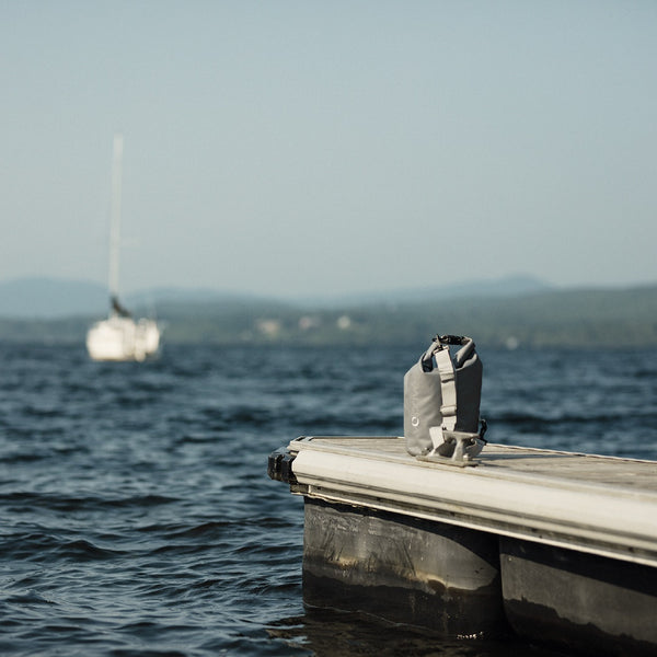 Sac au sec 5L gris de Volprivé sur quai lac Memphrémagog / Grey 5L dry bag on dock with sailboat by Volprivé.