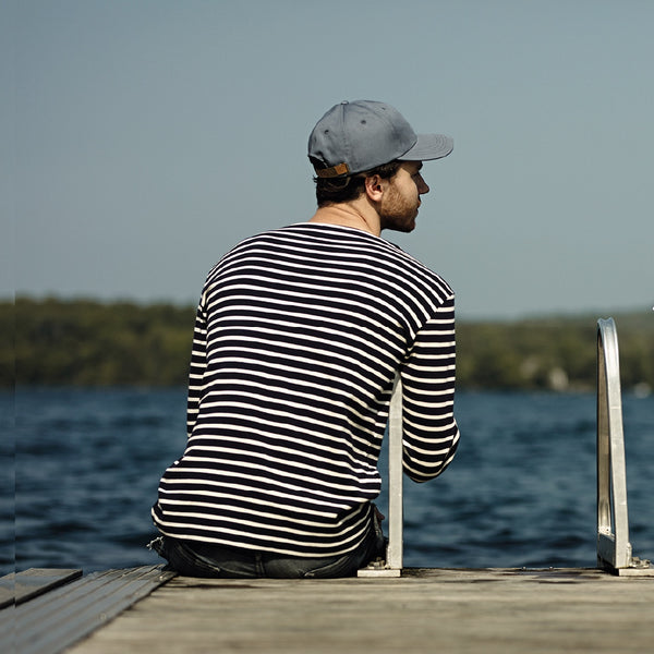 Jeune homme assis sur un quai au bord du lac avec casquette 100% coton bleue / Young women man sitting on dock near lake wearing a bluecap.