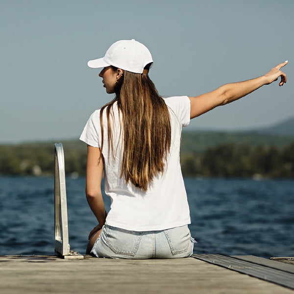 Jeune femme assise sur un quai au bord du lac avec casquette 100% coton blanche / Young women sitting on dock near lake wearing a white cap.