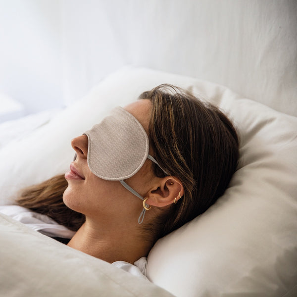 Jeune femme couchée sur un oreiller blanc avec masque de nuit beige / Young women asleep on white bed with night mask beige by Volprivé.