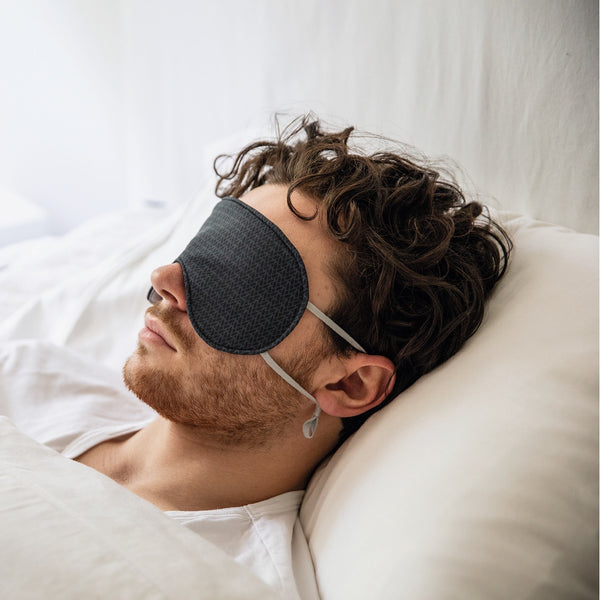 Jeune homme couché sur un oreiller blanc avec masque de nuit noir / Young man asleep on white bed with night mask black by Volprivé.