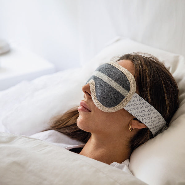 Jeune femme couchée dans un lit blanc avec masque de sommeil lesté gris et beige ajustable / Young women sleeping in white bed with weighted sleep mask in grey and beige made by Volprivé.