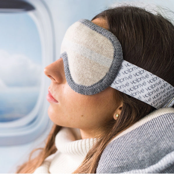 Jeune femme portant masque de sommeil lesté beige et gris en avion siège hublot / Young women wearing a beige and grey weighted sleep mask on plane window seat made by Volprivé.