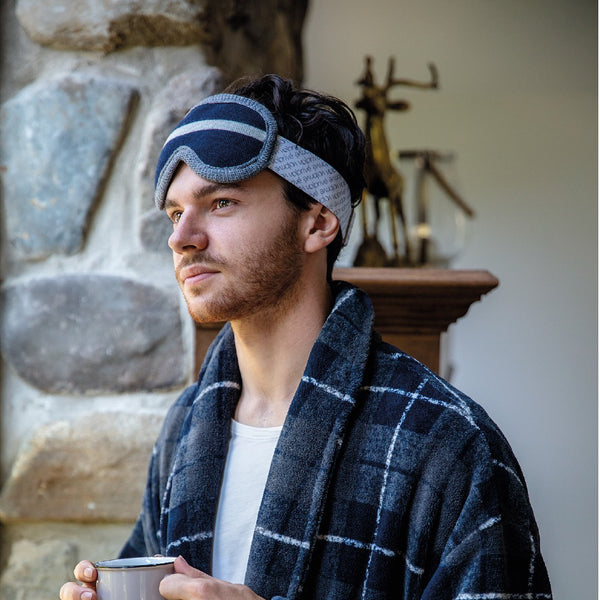 Jeune homme portant un masque de sommeil comme une lunette de ski bleu marine avec robe de chambre tasse de café à la main / Young man wearing a weighted sleep night mask on head like a ski goggle navy with bathrobe with coffee mug in hand by Volprivé.