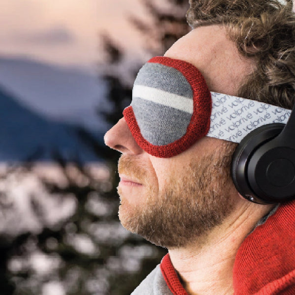 Homme portant masque de sommeil lesté gris et rouge dans décor lac et forêt / Man wearing a grey and red weighted sleep mask made by Volprivé.