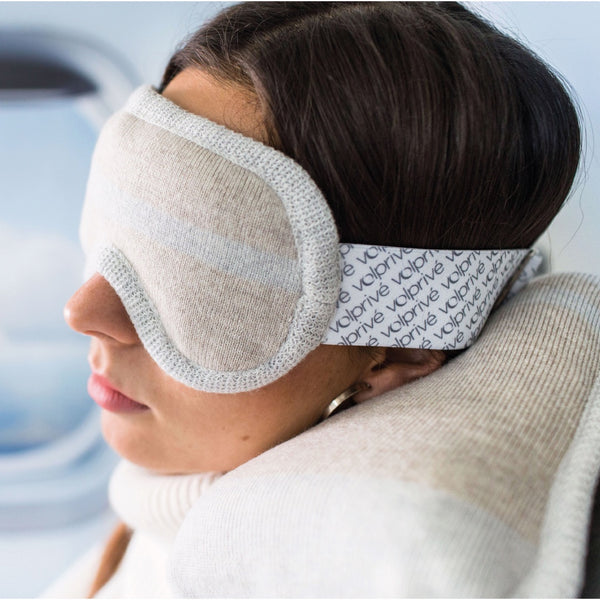 Jeune femme assise côté hublot avec masque et oreiller beige / Young women sitting in a plane wearing a sleep mask and travel pillow beige by Volprivé.