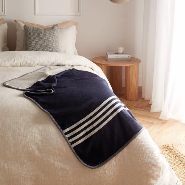 Jeté bleu marine avec 4 rayures blanches en laine de mérinos sur lit / Navy blue with 4 white stripes merino wool throw on bed made in Canada by Volprivé.