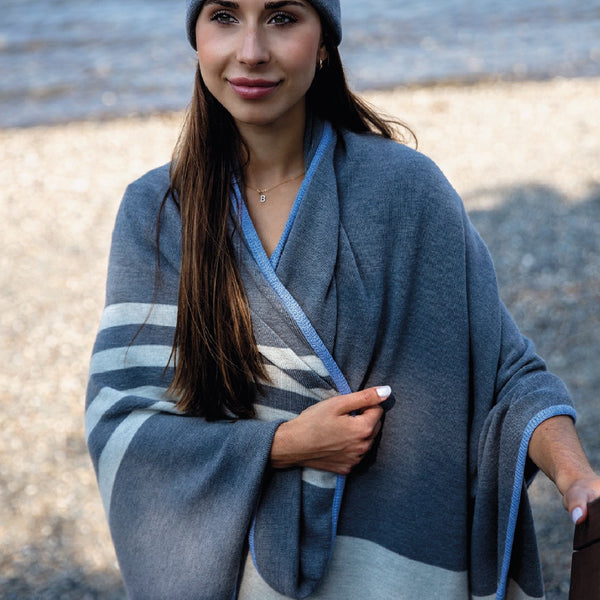 Couverture grise en laine de mérinos sur épaule d'une jeune femme sur plage / Grey blanket with white stripes merino wool blanket on shoulders of young women on beach.